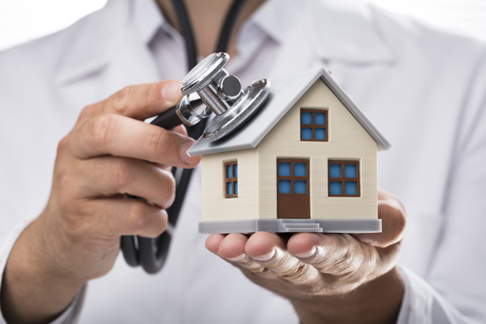 Profesional de la salud sosteniendo una casa en miniatura y un estetoscopio representando el servicio de hospitalización domiciliaria&nbsp;